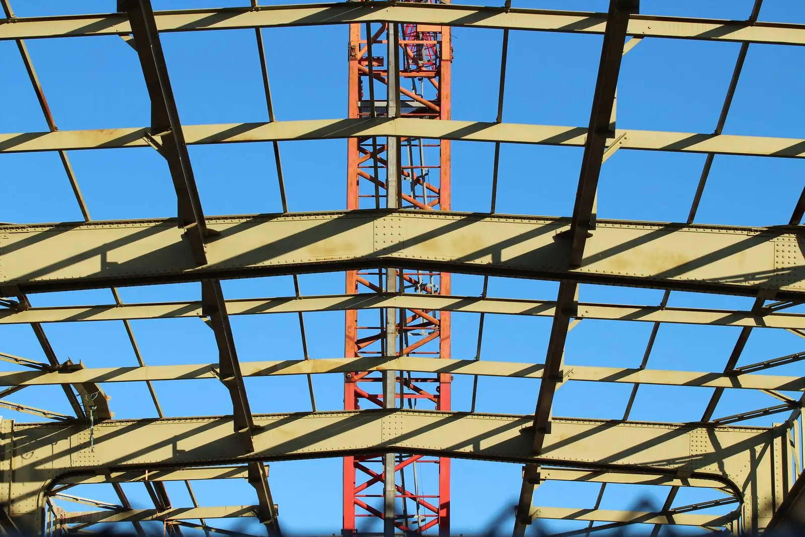 Steel roof framing seen from below against a blue sky